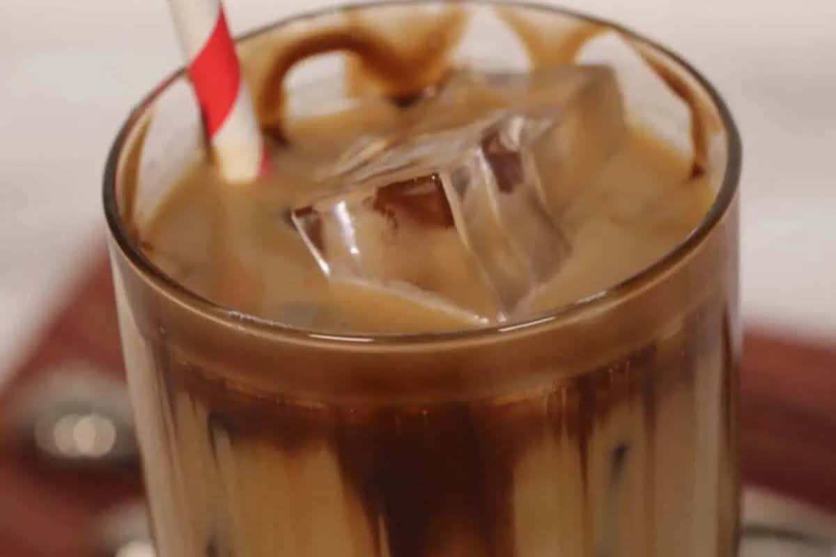 Close-up of an iced coffee drink with a red-and-white striped straw, chocolate syrup on the glass, and ice cubes floating on top—perfect to recreate your favorite Starbucks drinks at home.