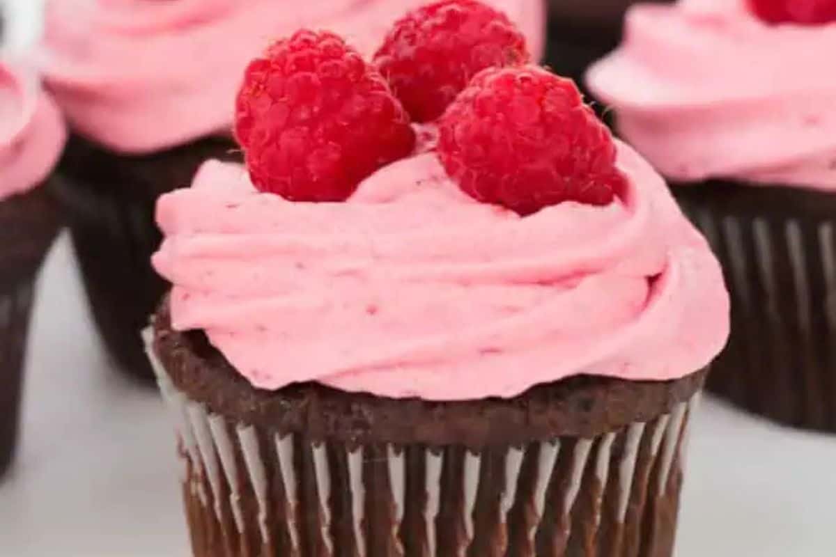 Indulge in a chocolate cupcake with pink frosting, adorned with three raspberries on top—a perfect Valentine dessert idea to wow your sweetheart!.