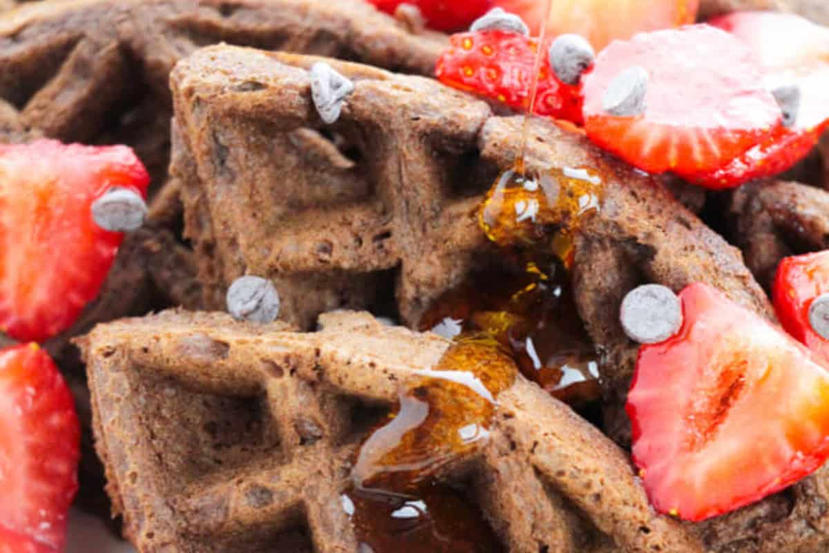 Close-up of chocolate waffles topped with sliced strawberries, chocolate chips, and maple syrup—the perfect way to indulge in your favorite chocolate recipes.