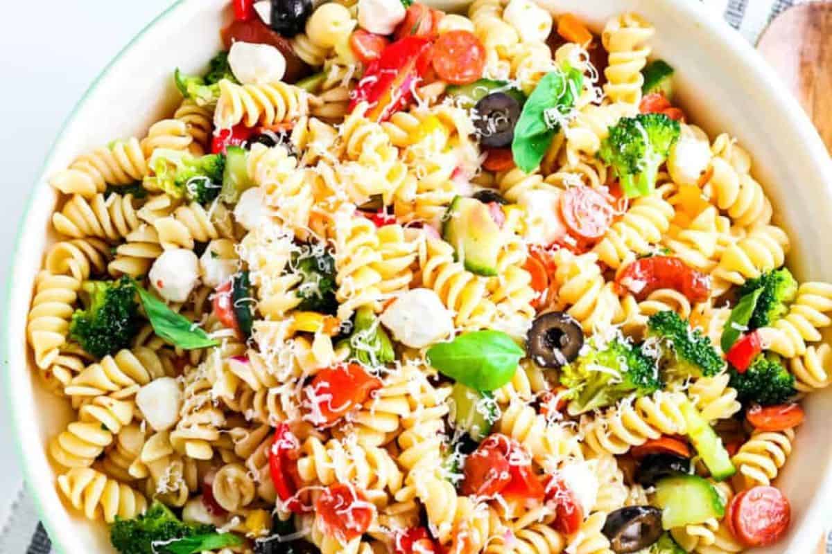 A bowl of rotini pasta salad mixed with broccoli, cherry tomatoes, olives, mozzarella balls, and pepperoni, garnished with basil and cheese—a perfect addition to your list of kid friendly dinner recipes.