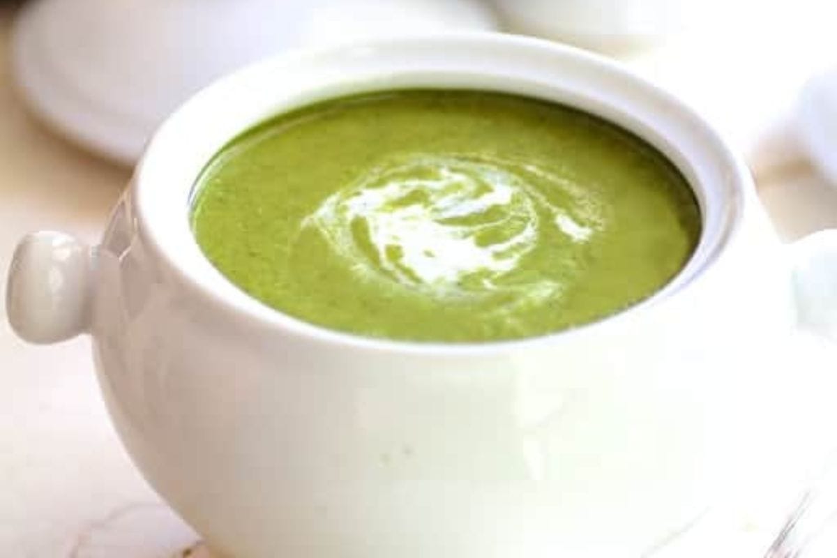 A white bowl filled with creamy green soup, topped with a swirl of cream—one of those Cozy Vegetable Soups perfect to warm up your day.