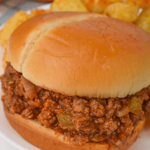 A close-up of a Crock Pot Sloppy Joe sandwich on a white plate, with diced potatoes in the background, effortlessly combining flavors for a hearty meal.