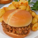 Crock Pot Sloppy Joe sandwich with a bun, ground beef filling, served on a plate with a side of golden tater tots and garnished with parsley.