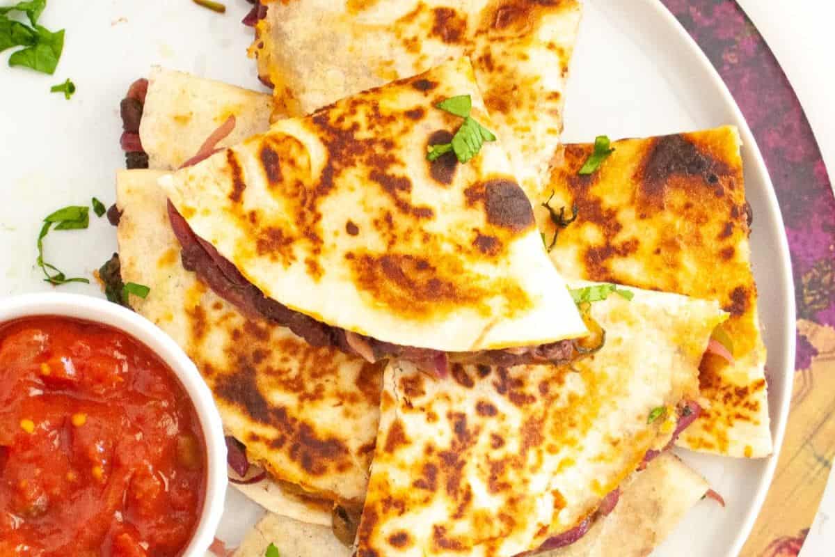 Quesadillas with melted cheese and beans, ready to score big at your Game Day Party. Served on a white plate with a small bowl of salsa beside them, these Touchdown Treats are sure to be a hit.