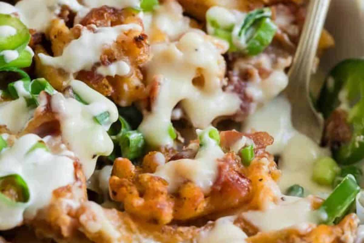 Close-up of loaded fries topped with melted cheese, bacon bits, and sliced green onions—a true touchdown treat for your game day party. A fork is partially visible in the background.