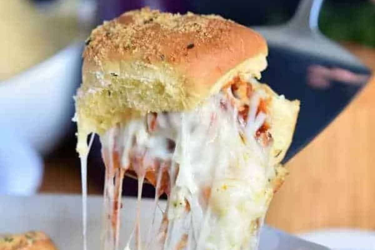 Close-up of irresistible meatball sliders with melted cheese and toppings, being lifted from a tray with a spatula—perfect for game day snacking.