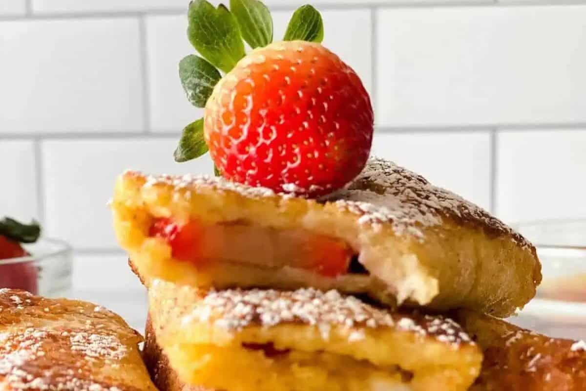 Close-up of powdered sugar-dusted pastries filled with strawberry, topped with a whole fresh strawberry—a perfect treat for weekend brunch or lazy morning recipes, set against a white tile background.