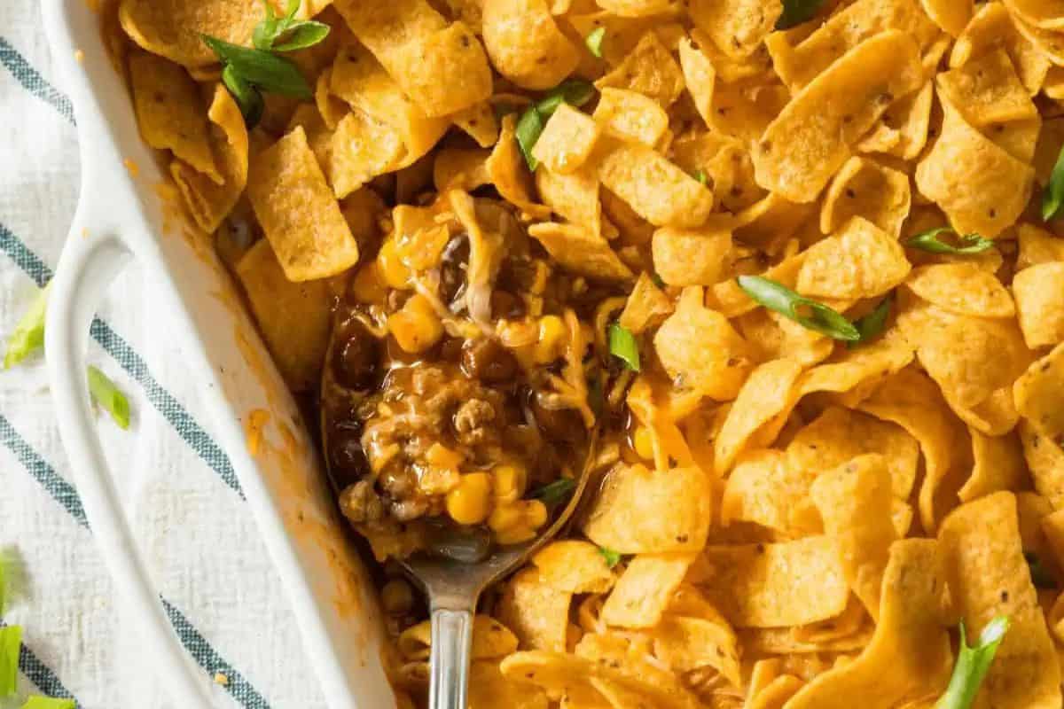 A dish of cheesy Frito pie, perfect for a Game Day Party, topped with corn chips and sliced green onions, with a spoon scooping a portion.