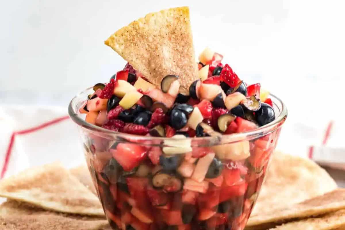 A glass bowl filled with diced strawberries, blueberries, and apples topped with a cinnamon-sugar tortilla chip is the perfect dip to score big points at your Super Bowl party.
