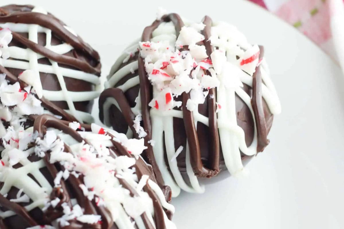 Indulge in three chocolate truffles drizzled with white chocolate and sprinkled with crushed peppermint candy, beautifully displayed on a white surface.