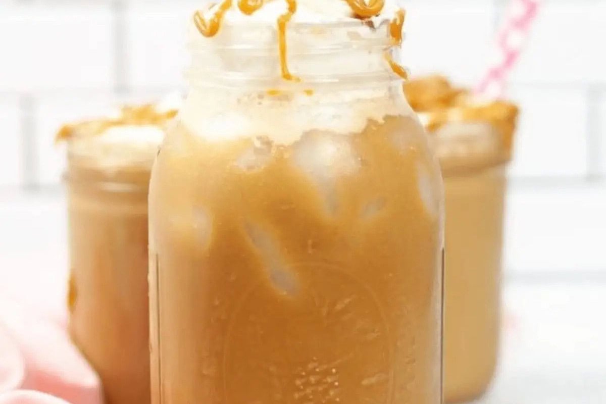A mason jar filled with iced coffee topped with whipped cream and caramel drizzle, inspired by Starbucks drinks you can easily recreate at home, with two similar jars in the background.