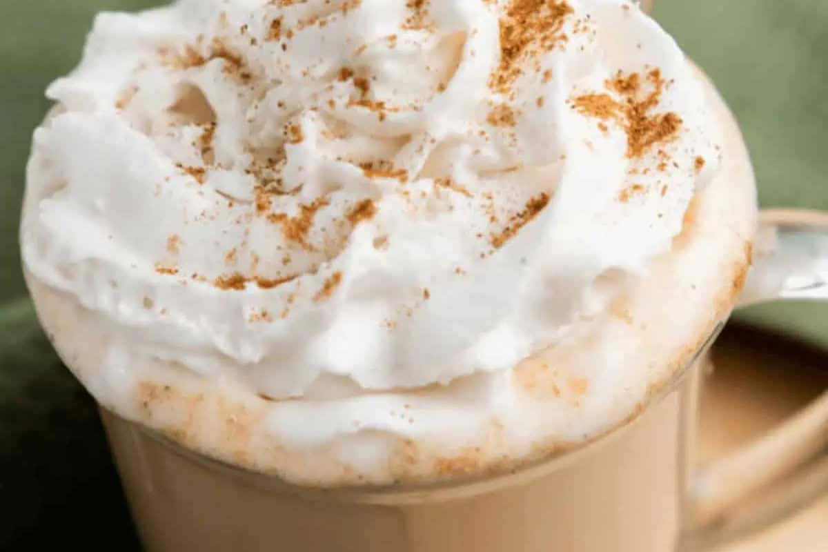 A glass mug filled with coffee topped with whipped cream and a sprinkle of cinnamon—perfect to recreate at home for those who love Starbucks drinks.