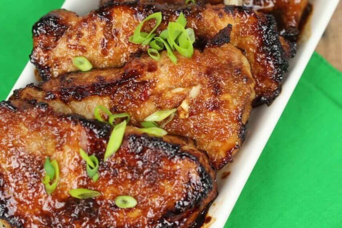Close-up of some glazed korean pork chops, served on a rectangular white plate.
