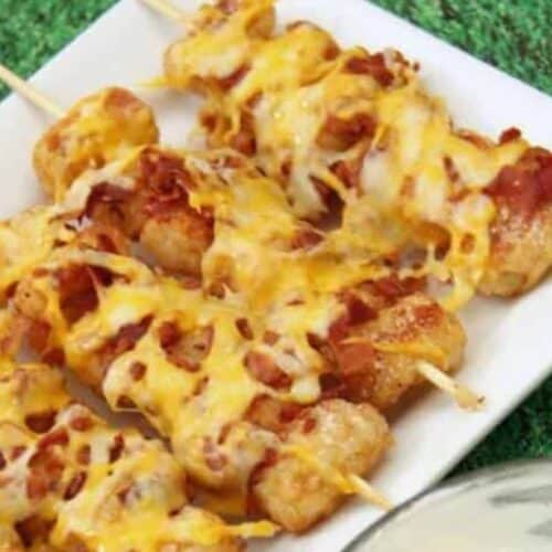 Skewered tater tots topped with melted cheese and bacon make the perfect Touchdown Treats on a white rectangular plate.