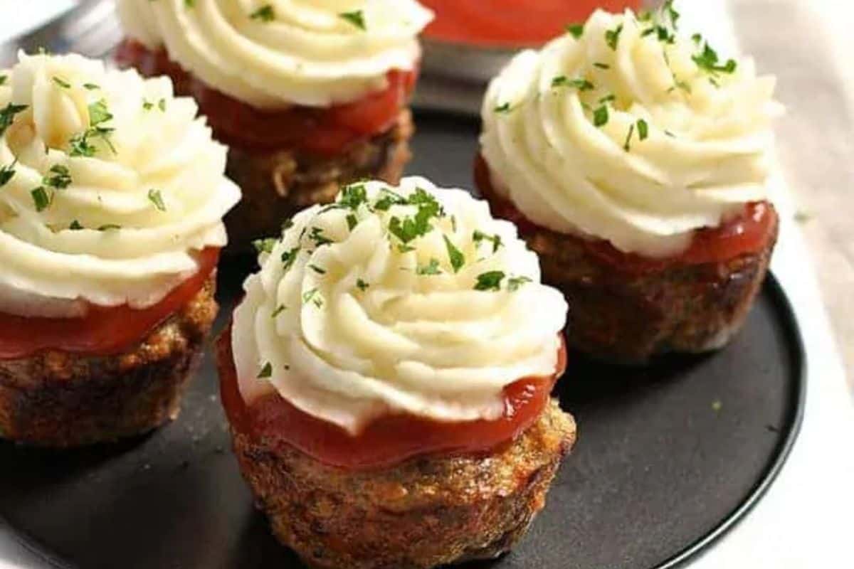 Mini meatloaf cupcakes topped with piped mashed potatoes and parsley, arranged on a serving tray.