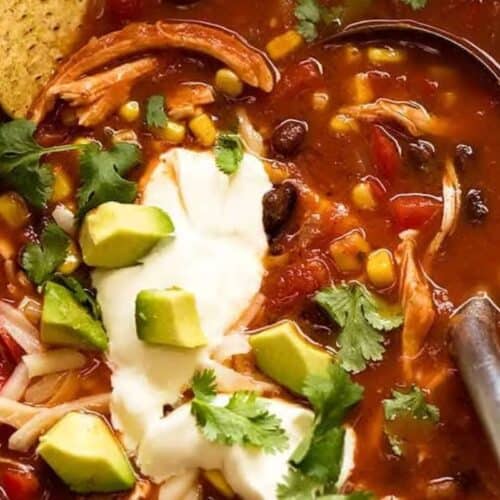 A bowl of chicken tortilla soup topped with avocado, sour cream, shredded cheese, cilantro, corn, black beans, and a tortilla chip—one of those cozy soups perfect for busy nights.