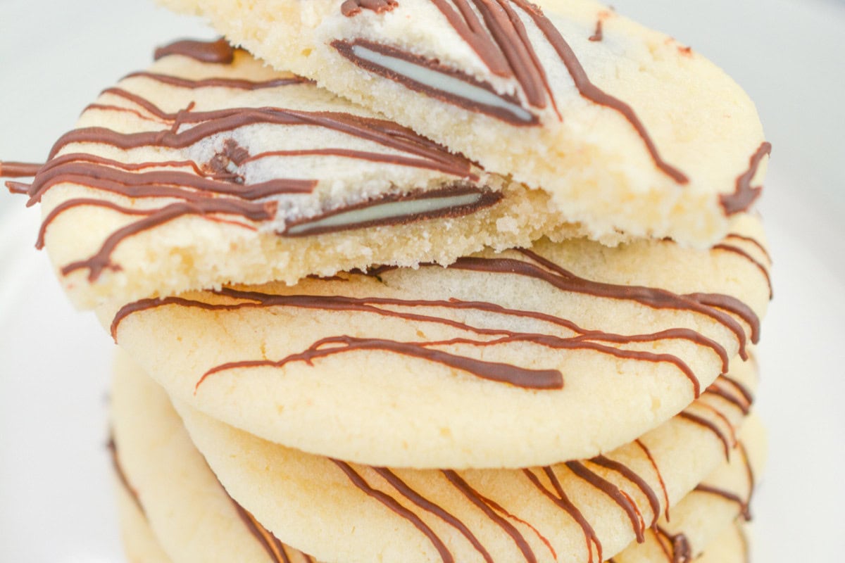 Indulge in a stack of round sugar cookies drizzled with chocolate, with the top cookie broken in half to reveal a rich chocolate filling inside.