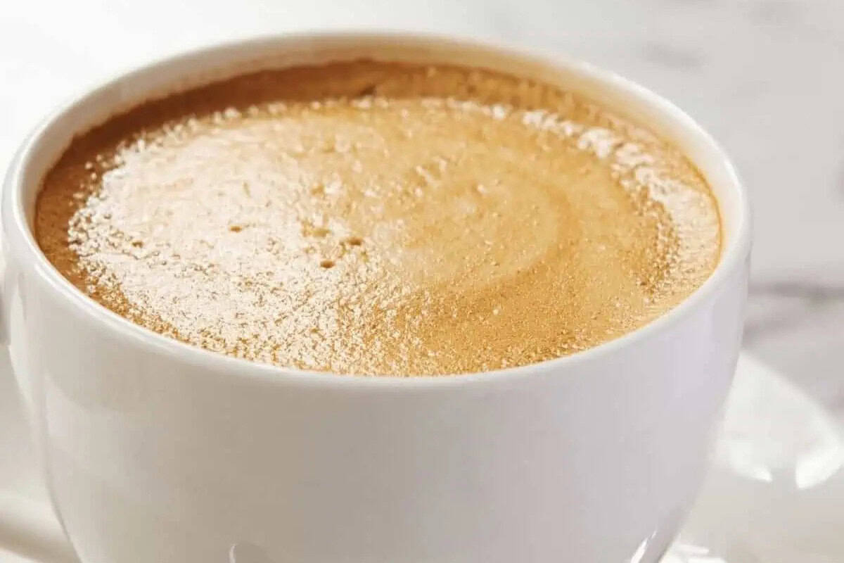 A close-up of a white cup filled with coffee topped with a layer of frothy crema—perfect inspiration to recreate at home using your favorite Starbucks recipes.