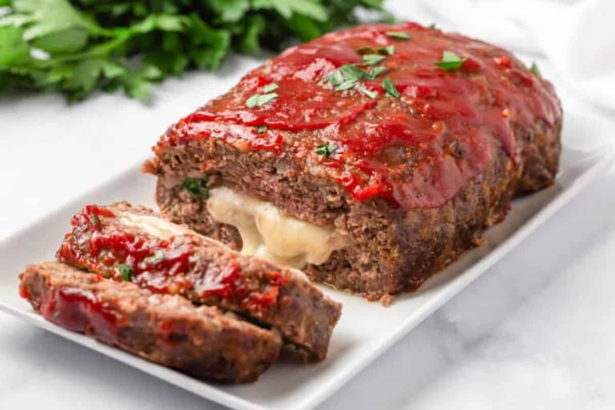 Cross-section of stuffed meatloaf showing melted cheese inside, garnished with chopped parsley.