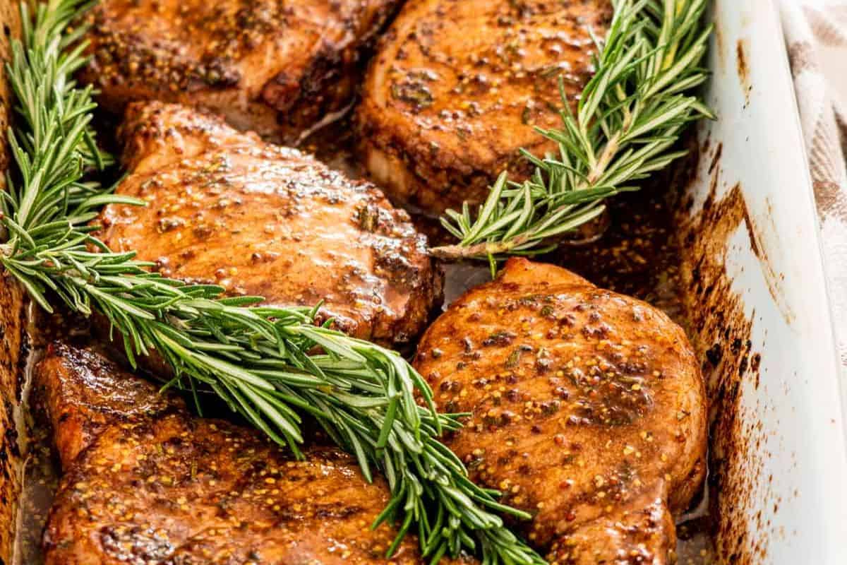 Close-up of some mustard balsamic pork chops served in a white dish and topped with rosemary.