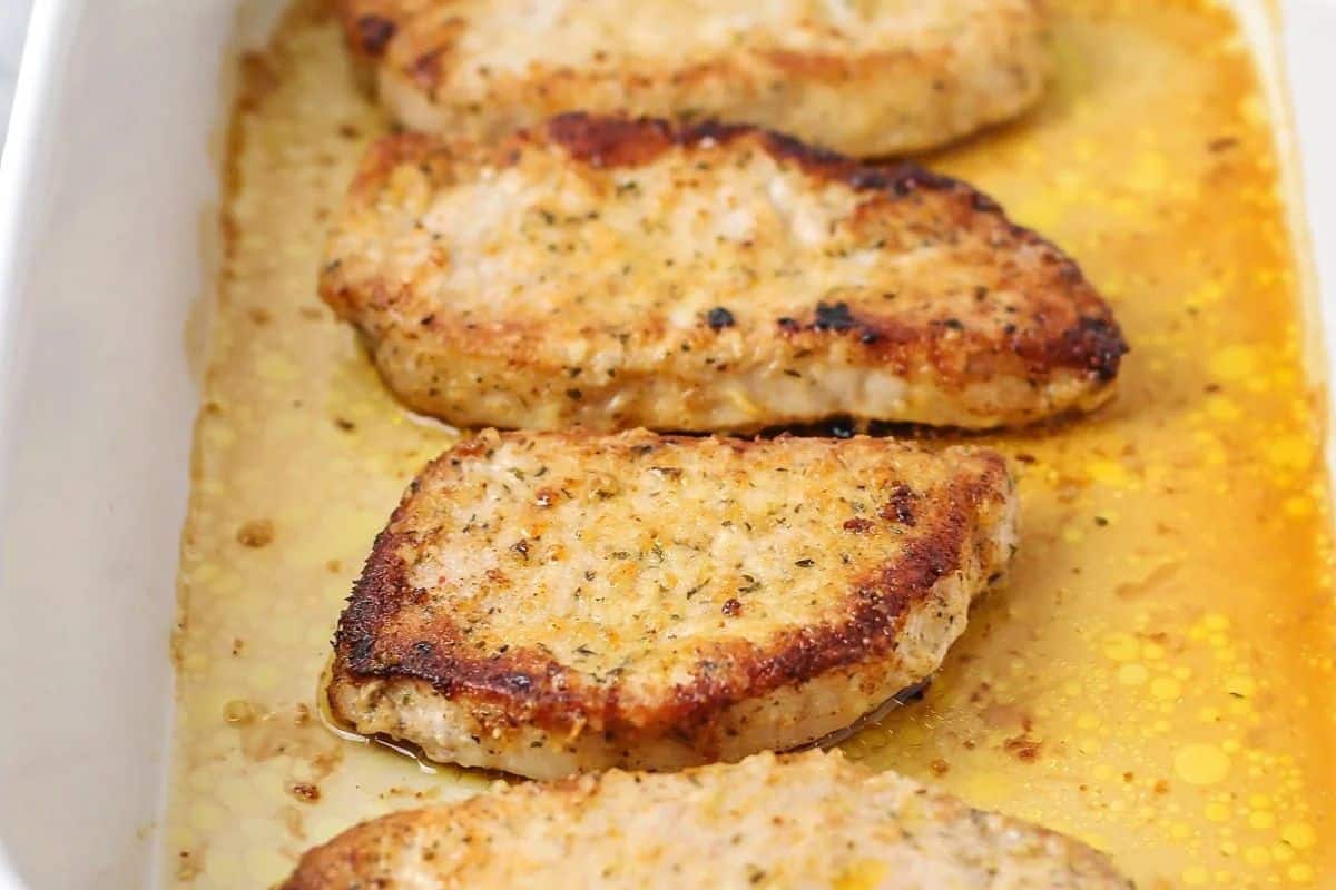 Close-up of some parmesan crusted pork chops, served in a white baking dish.