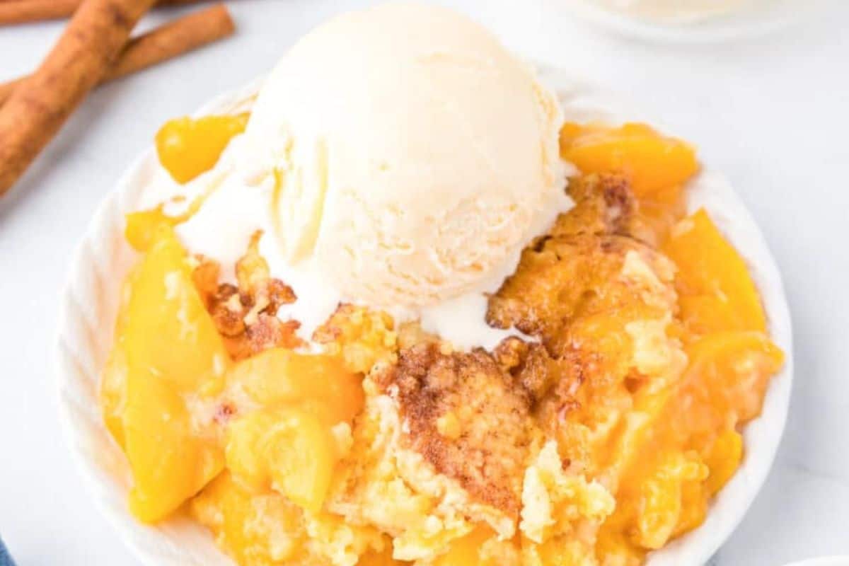 Close-up of a slice of peach dump cake, served on a white plate and topped with vanilla ice cream.