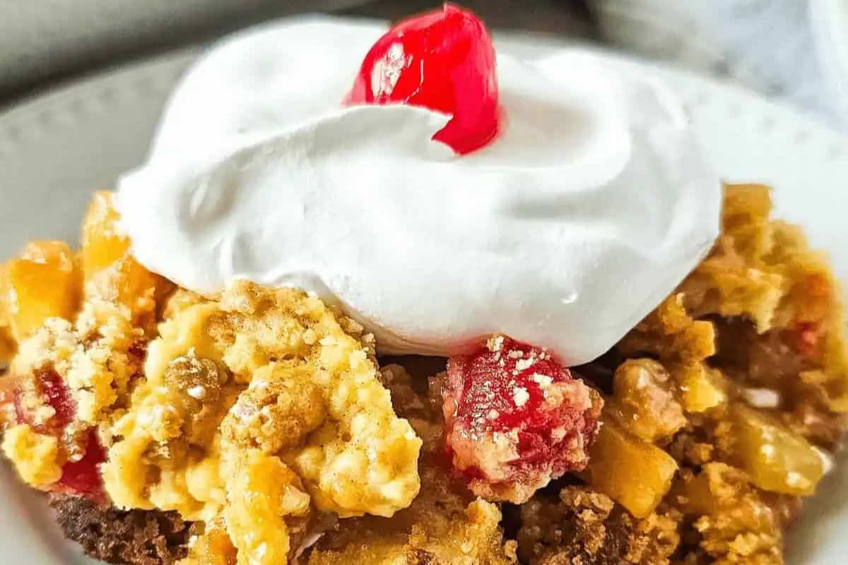 Close-up of a slice of pineapple dump cake, topped with wipped cream and a cherry.