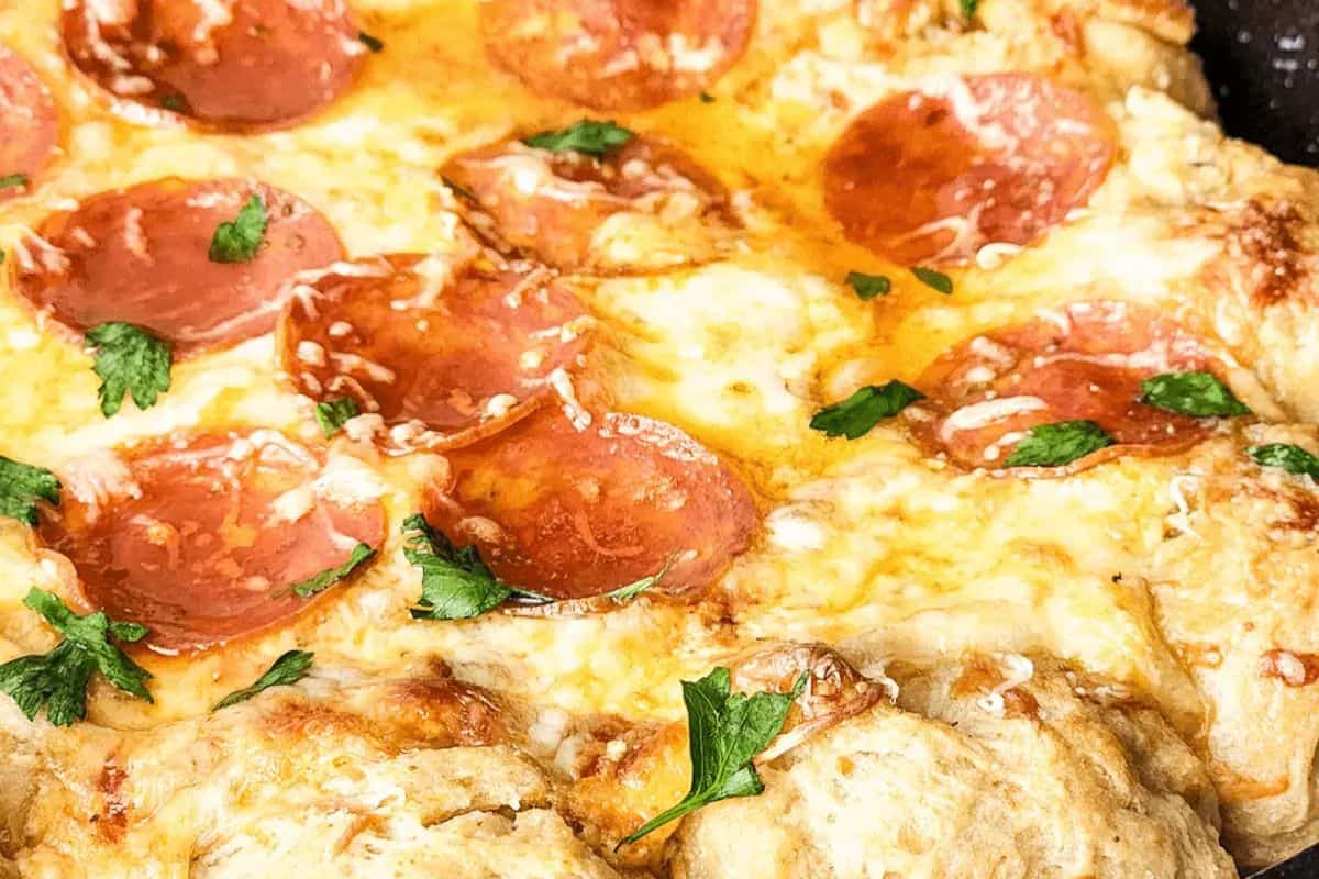 Close-up of a pizza with pepperoni slices, melted cheese, and sprinkled herbs on a thick crust—score big points at your Super Bowl party with this delicious spread.