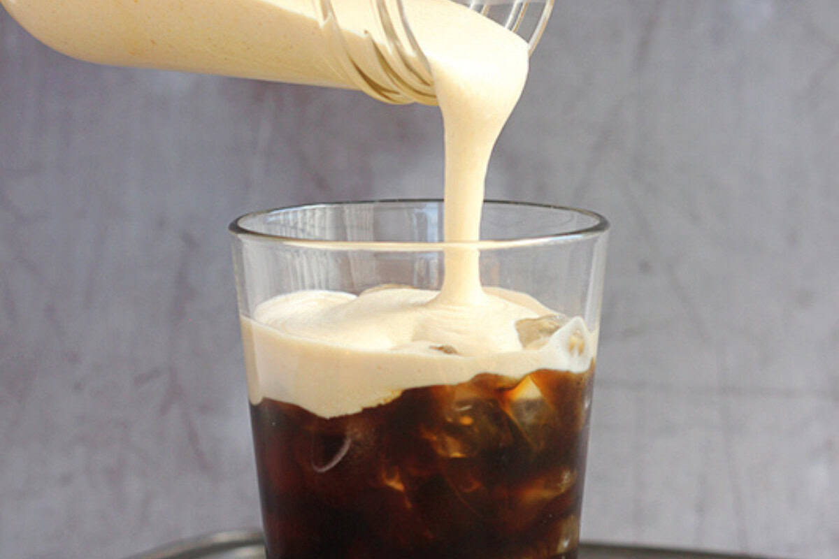 A glass of iced coffee is being topped with a thick layer of creamy foam poured from a jar, perfect for those who want to recreate Starbucks drinks at home.