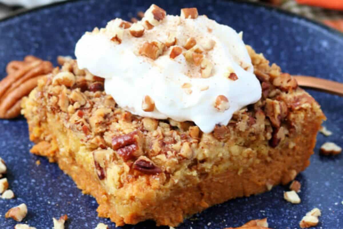 Close-up of a slice of pumpkin dump cake, topped with wipped cream and pecan bits.