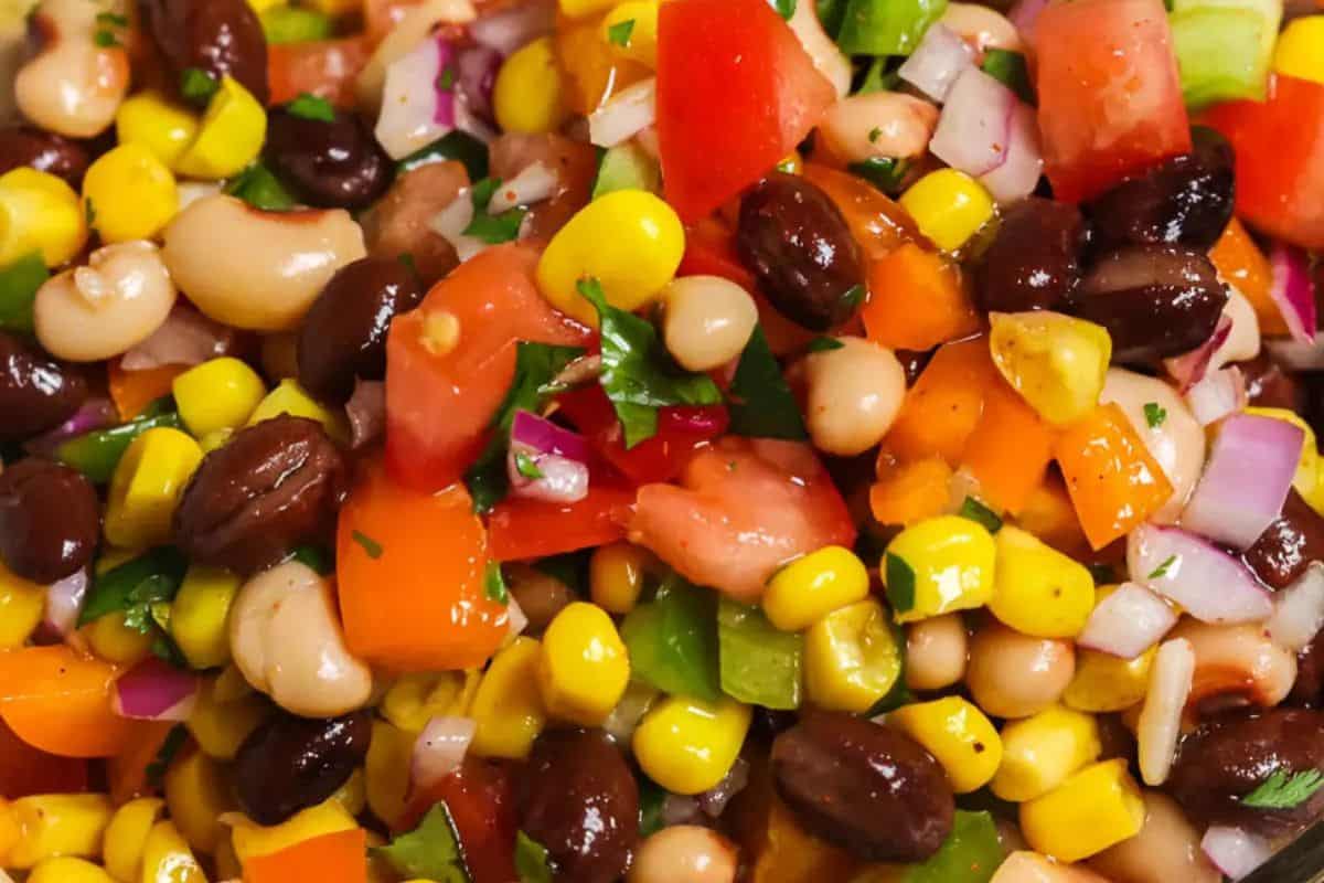 Close-up of a colorful salad featuring corn, black beans, white beans, tomatoes, red onion, and bell peppers, garnished with chopped herbs. This dish is sure to score big points at any gathering.