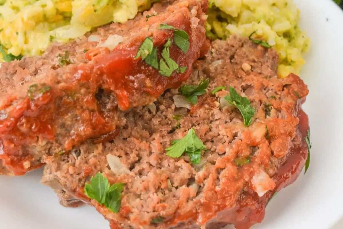 Sliced meatloaf topped with ketchup glaze, served with some yellow rice, made with Ritz crackers for extra flavor.