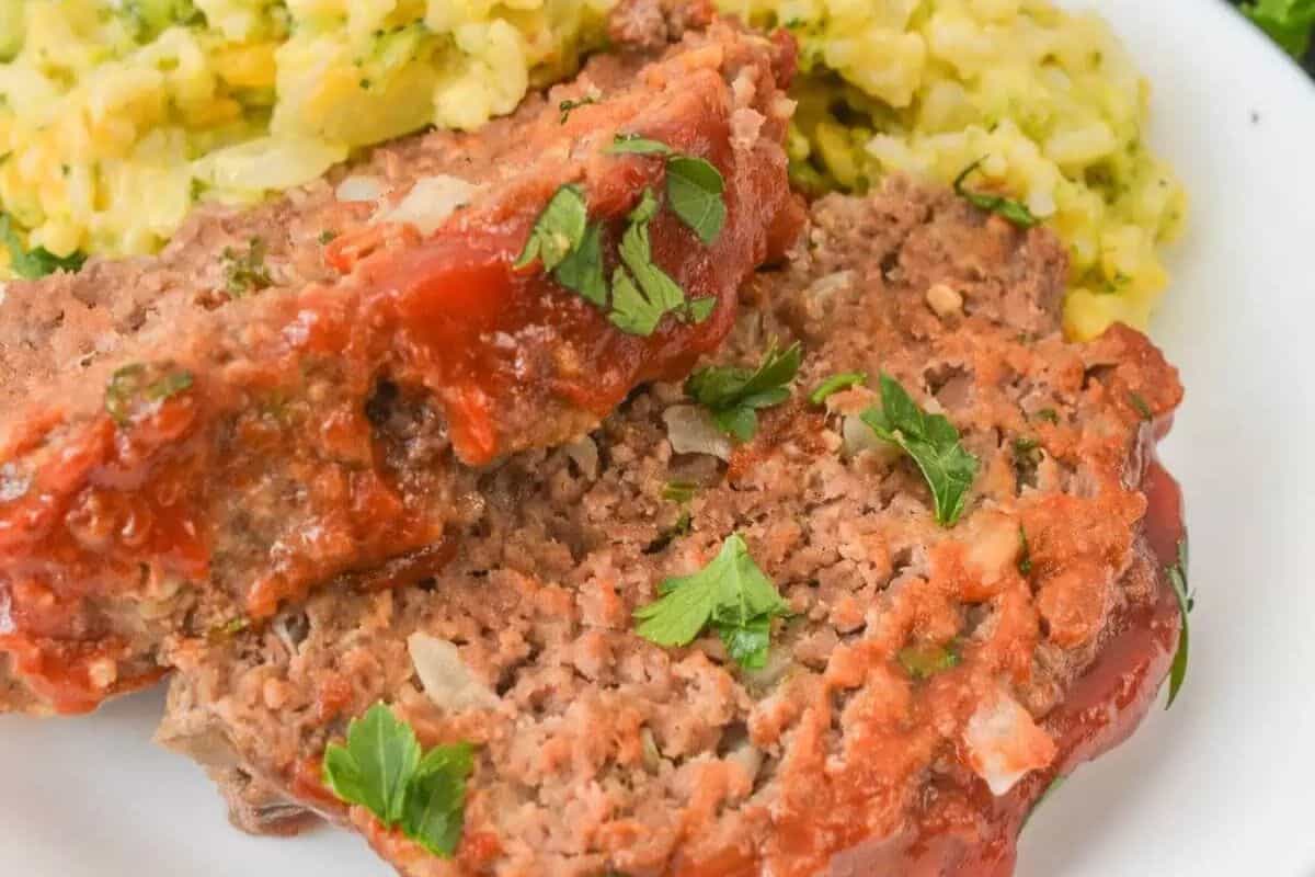 Two slices of meatloaf topped with tomato sauce and parsley, served with yellow rice on a white plate—perfect for kid friendly dinners that everyone will love.