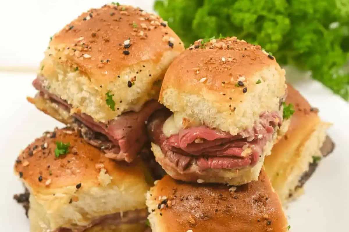 A stack of irresistible sliders with roast beef and melted cheese on seasoned buns, perfect for game day. Parsley garnish in the background.