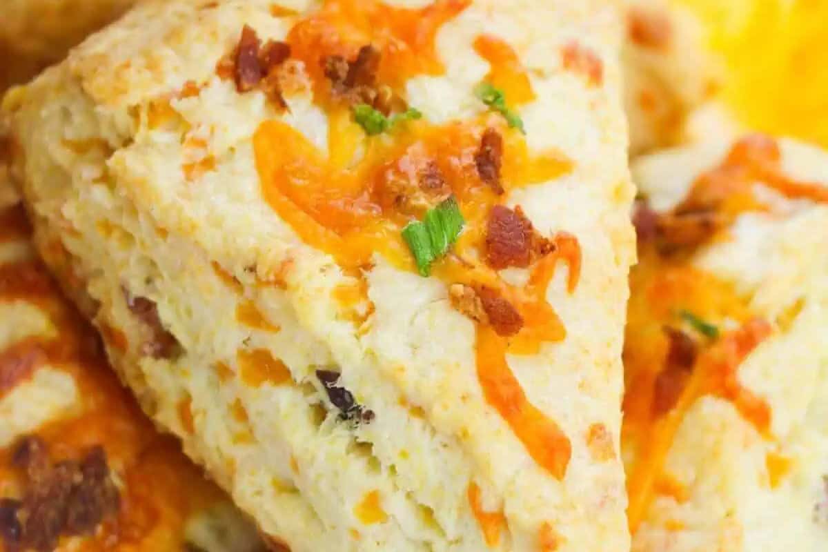 A close-up of a savory cheddar biscuit topped with melted cheese, bacon bits, and chopped green onions—perfect for lazy brunch or weekend mornings.
