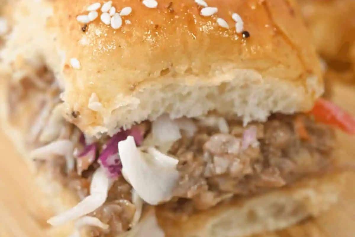 Close-up of irresistible sliders featuring shredded pork, onions, and cabbage piled high on a sesame seed bun—the perfect bite for Game Day.