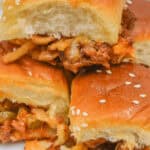 Three savory sliders with sesame seeds and onions on buns are stacked like delicious Sloppy Joe Sliders on a plate.