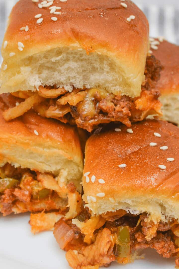 Three savory sliders with sesame seeds and onions on buns are stacked like delicious Sloppy Joe Sliders on a plate.