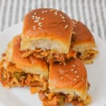 A stack of four sandwiches with sesame seed buns sits invitingly on a white plate, placed atop a striped cloth.