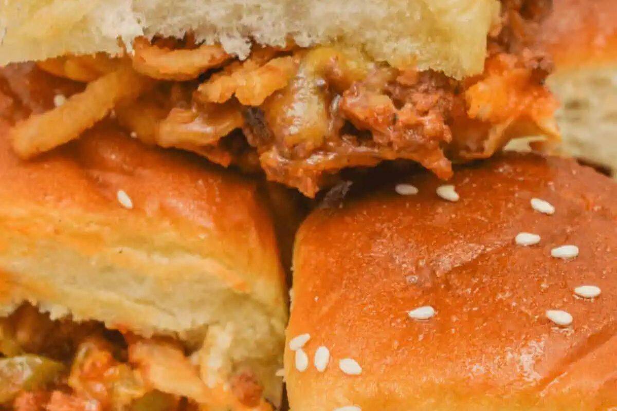 A close-up of a sloppy joe slider, showing the top bun lifted slightly to reveal the meaty, saucy filling with some crispy fried onions.