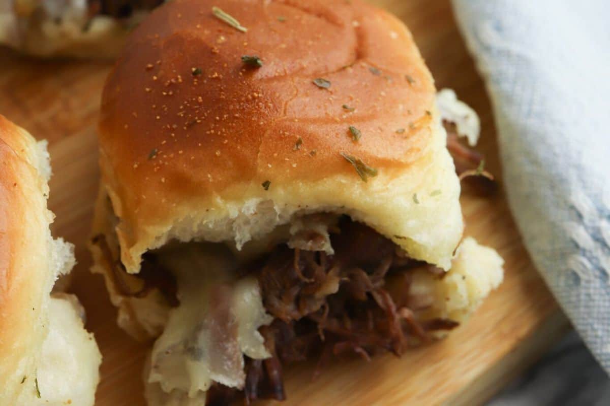 A close-up of an irresistible beef Italian slider on a wooden board, perfect for Game Day. The soft bun cradles the shredded pork filling, topped with a sprinkle of herbs.