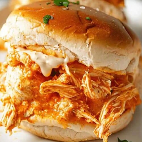 A shredded chicken slider with sauce on a bun, garnished with small green herbs, served on a white plate—perfect for Game Day.