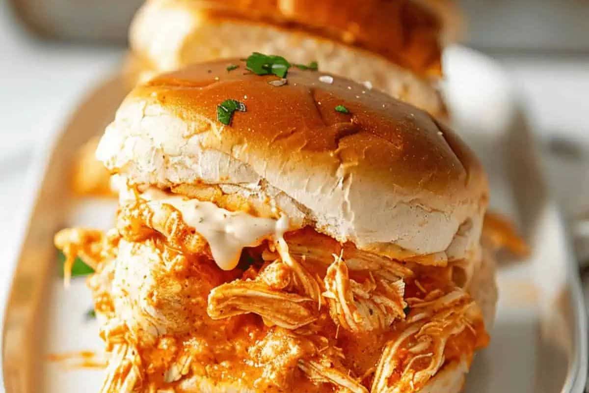 A close-up of a slider bun filled with shredded buffalo chicken and a drizzle of white sauce.
