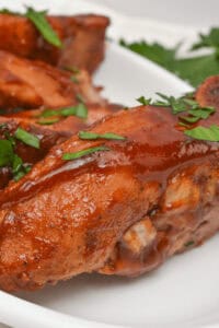 Close-up of succulent slow cooker country style ribs garnished with chopped herbs on a white plate.