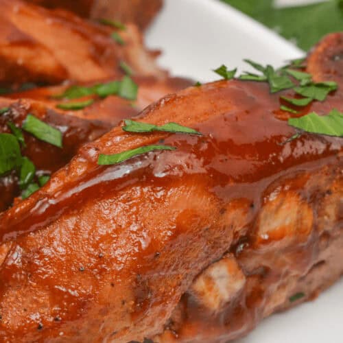 Close-up of succulent slow cooker country style ribs garnished with chopped herbs on a white plate.