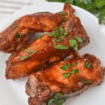 Slow-cooked, country-style ribs are tender and juicy, covered in rich sauce and garnished with chopped herbs on a white plate.