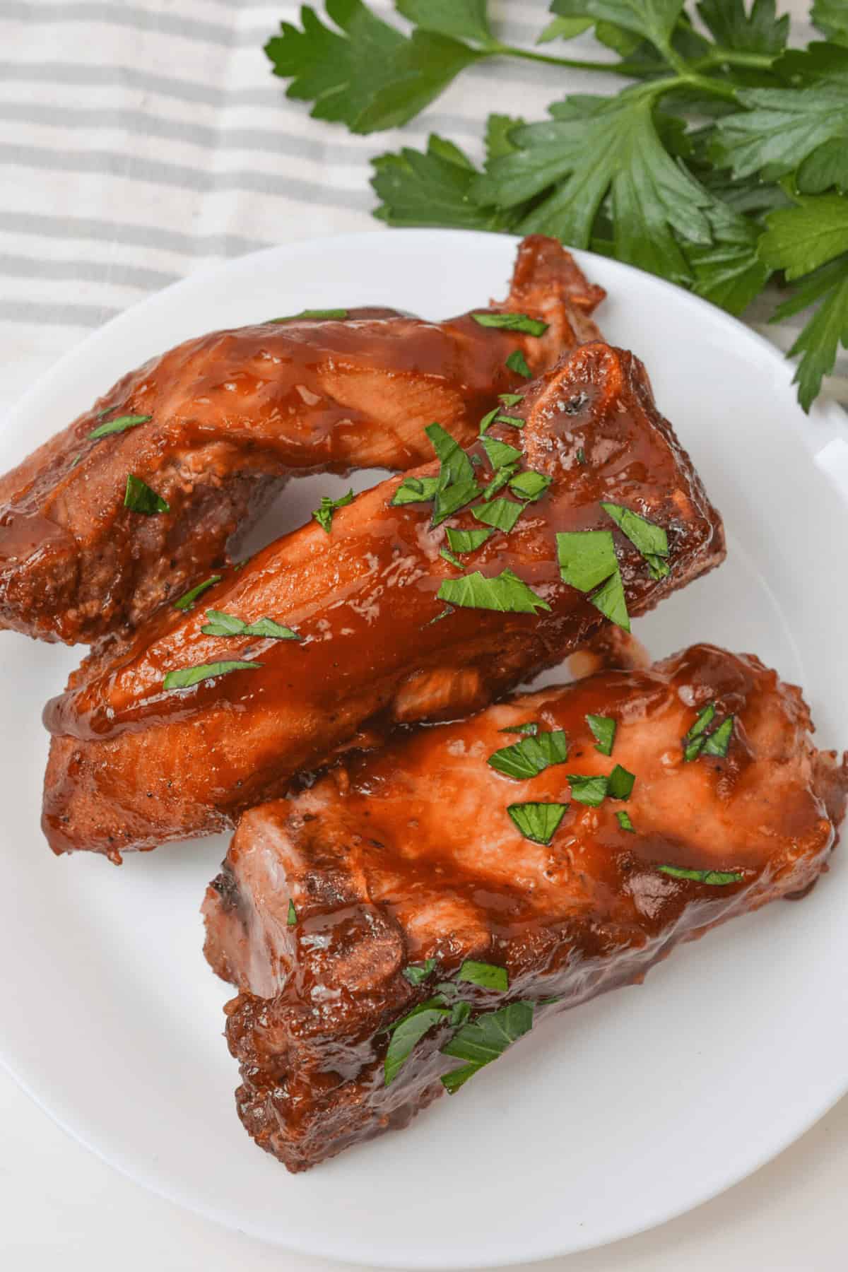 Slow-cooked, country-style ribs are tender and juicy, covered in rich sauce and garnished with chopped herbs on a white plate.