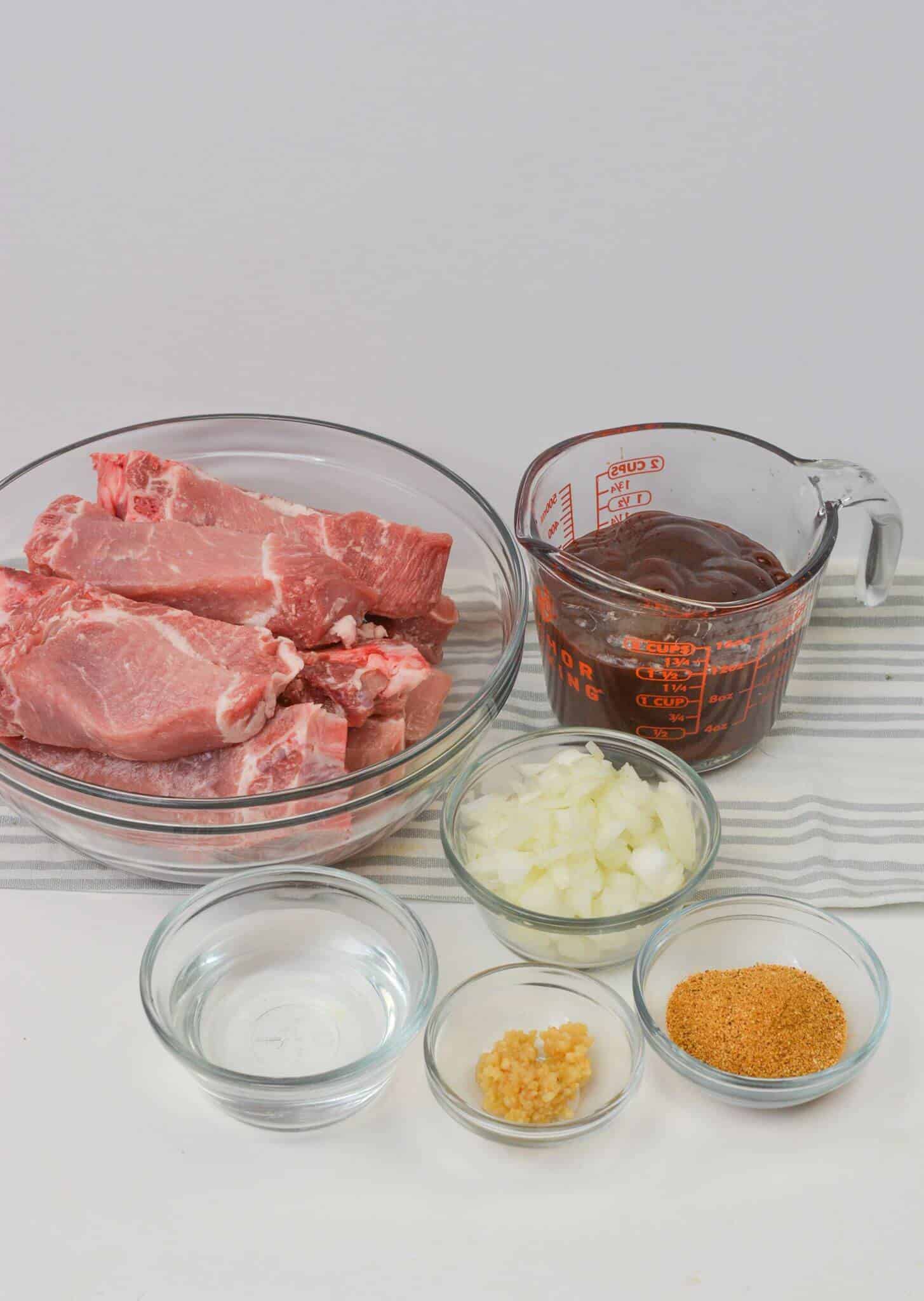 The meat in a bowl, barbecue sauce in a measuring cup, diced onions, minced garlic, and seasoning mix.