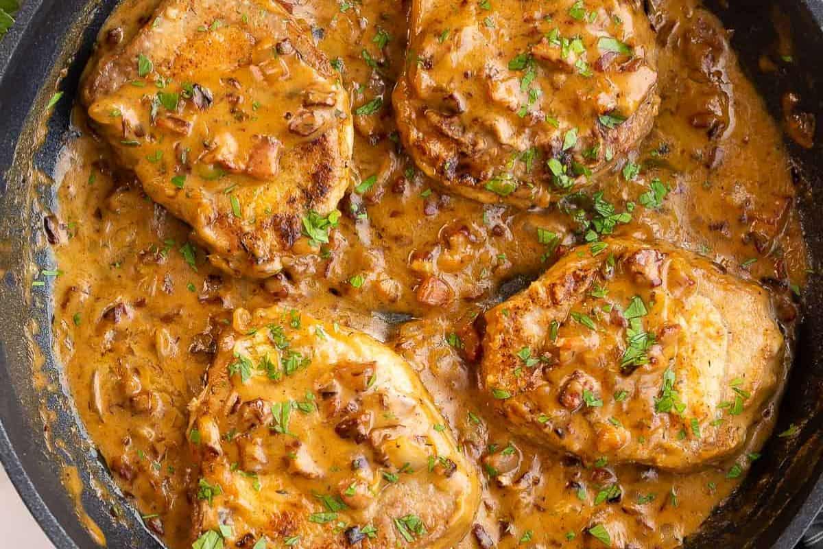 Close-up of smothered pork chops, served in a black baking dish coated with a savory gravy.