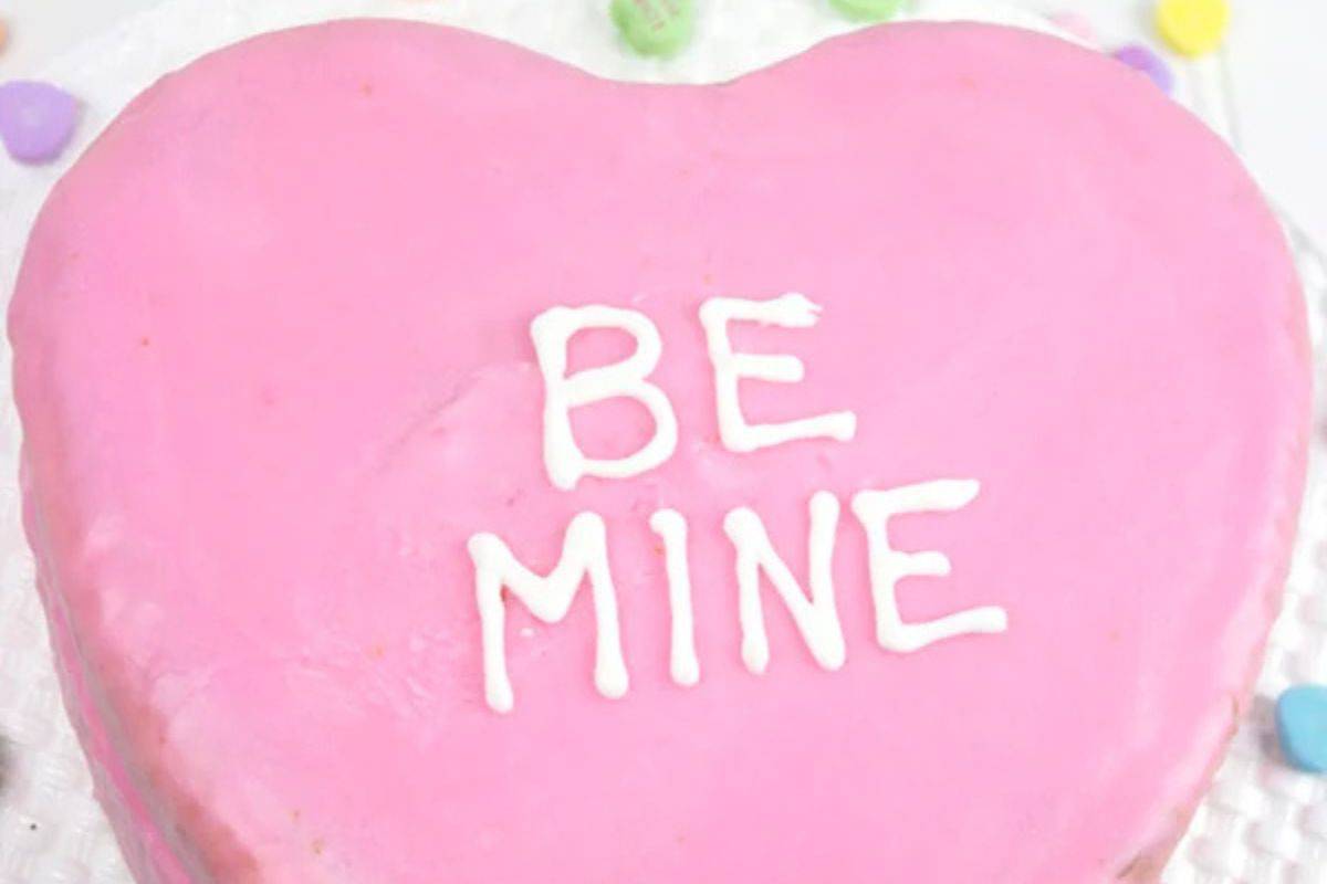 A heart-shaped pink cake with "BE MINE" inscribed in white icing showcases an adorable Valentine's dessert idea, sure to impress your sweetheart. Wow your loved one with this romantic and delicious creation that perfectly captures the essence of affection.
